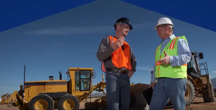 2 men talking in front of heavy equipment